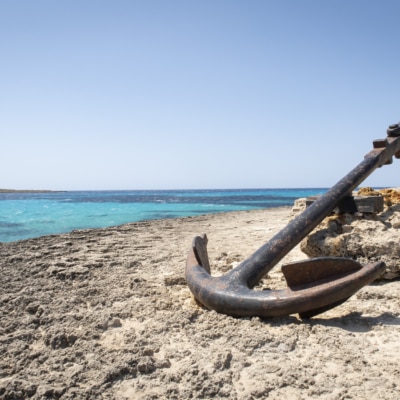 A Large Old Anchor, Stranded On A Rocky Cliff With A Sea Of Turquoise Water, Copy Space